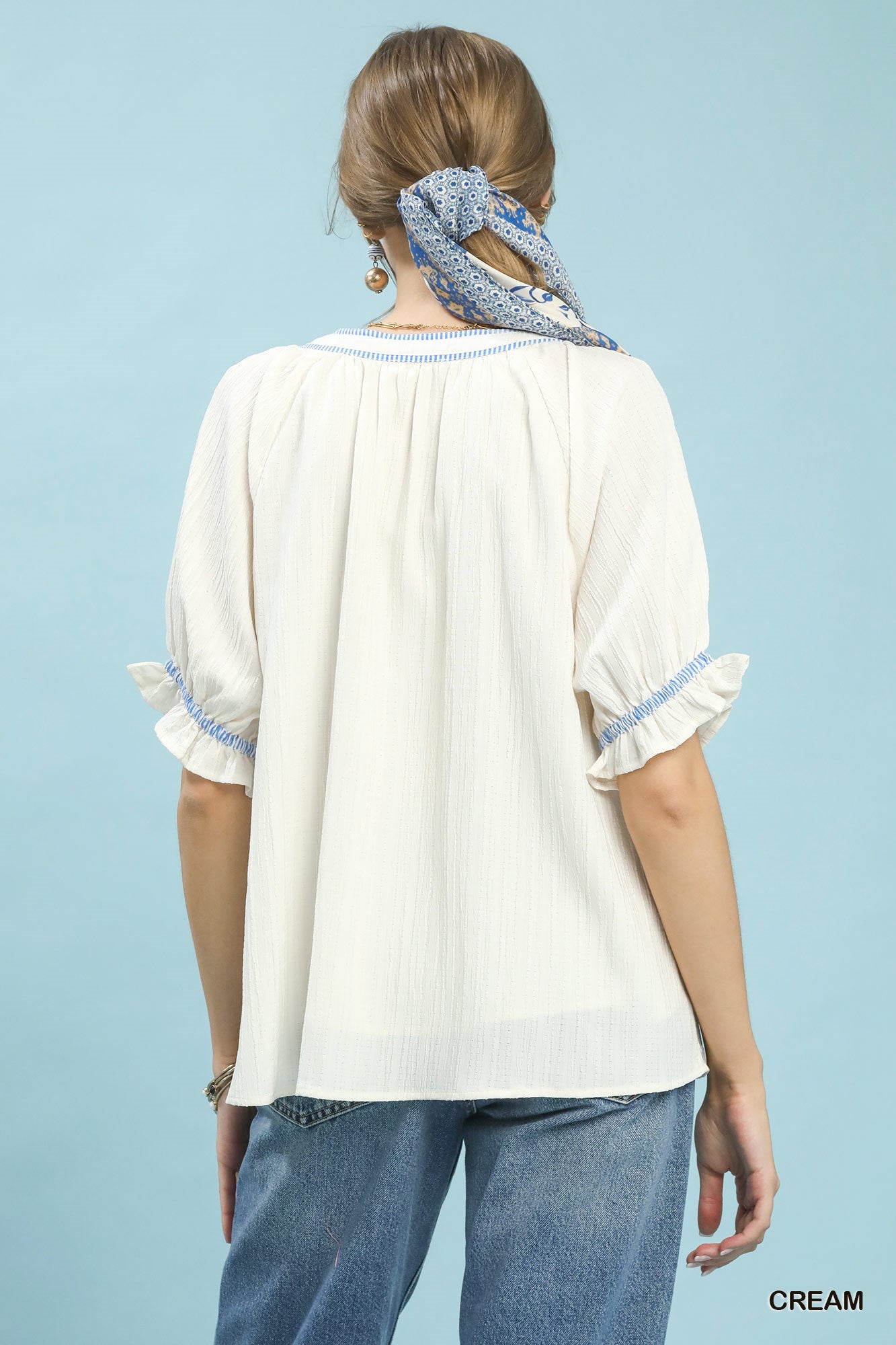 Woman wearing a cream blouse with blue trim against a light blue background