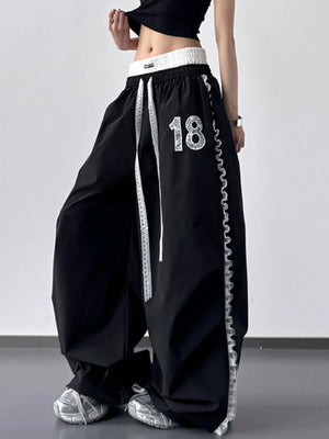 Black wide-leg pants with white stripes and number '18' on a plain background