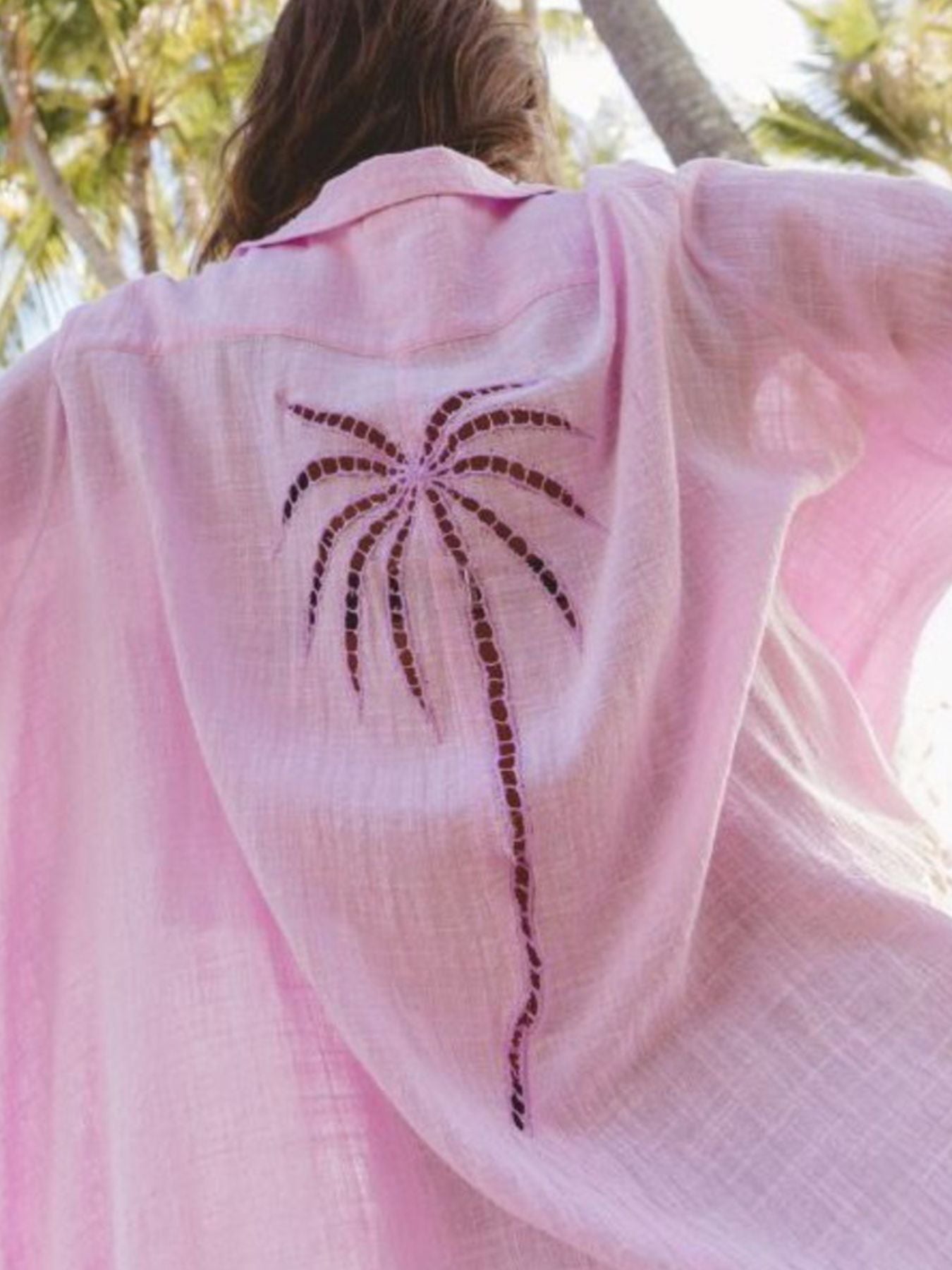 Pink garment with a palm tree design draped over a person, outdoors.