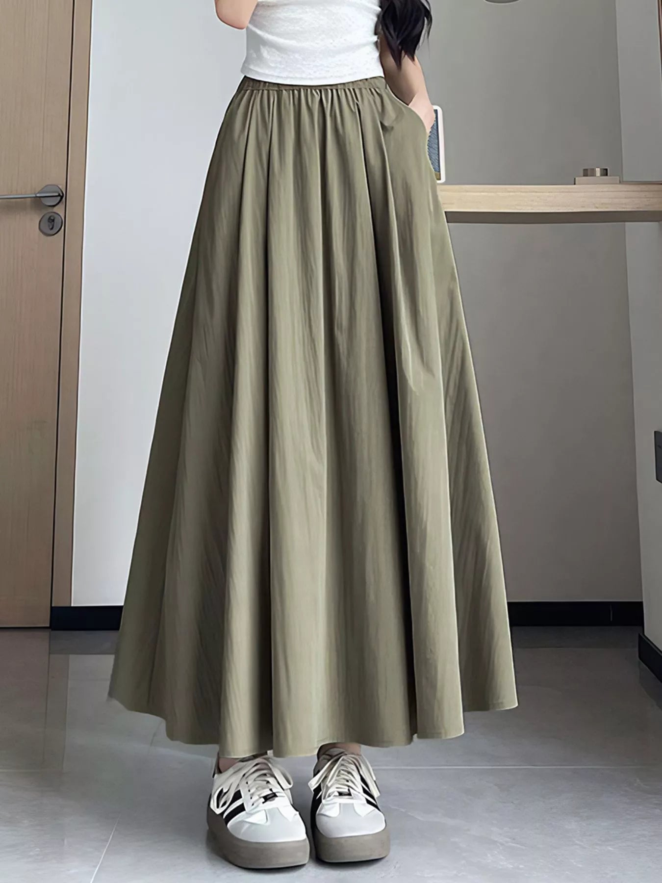 Person wearing a long olive green skirt with white sneakers indoors.