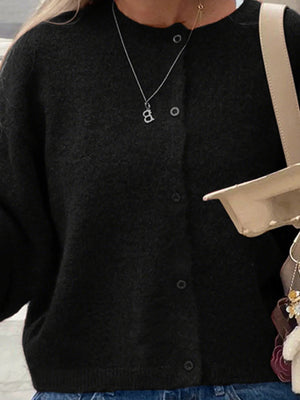 Person wearing a black cardigan with a necklace, holding a beige handbag.