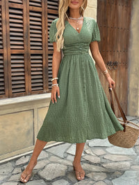 Woman in a green dress standing on a stone path with wooden shutters in the background
