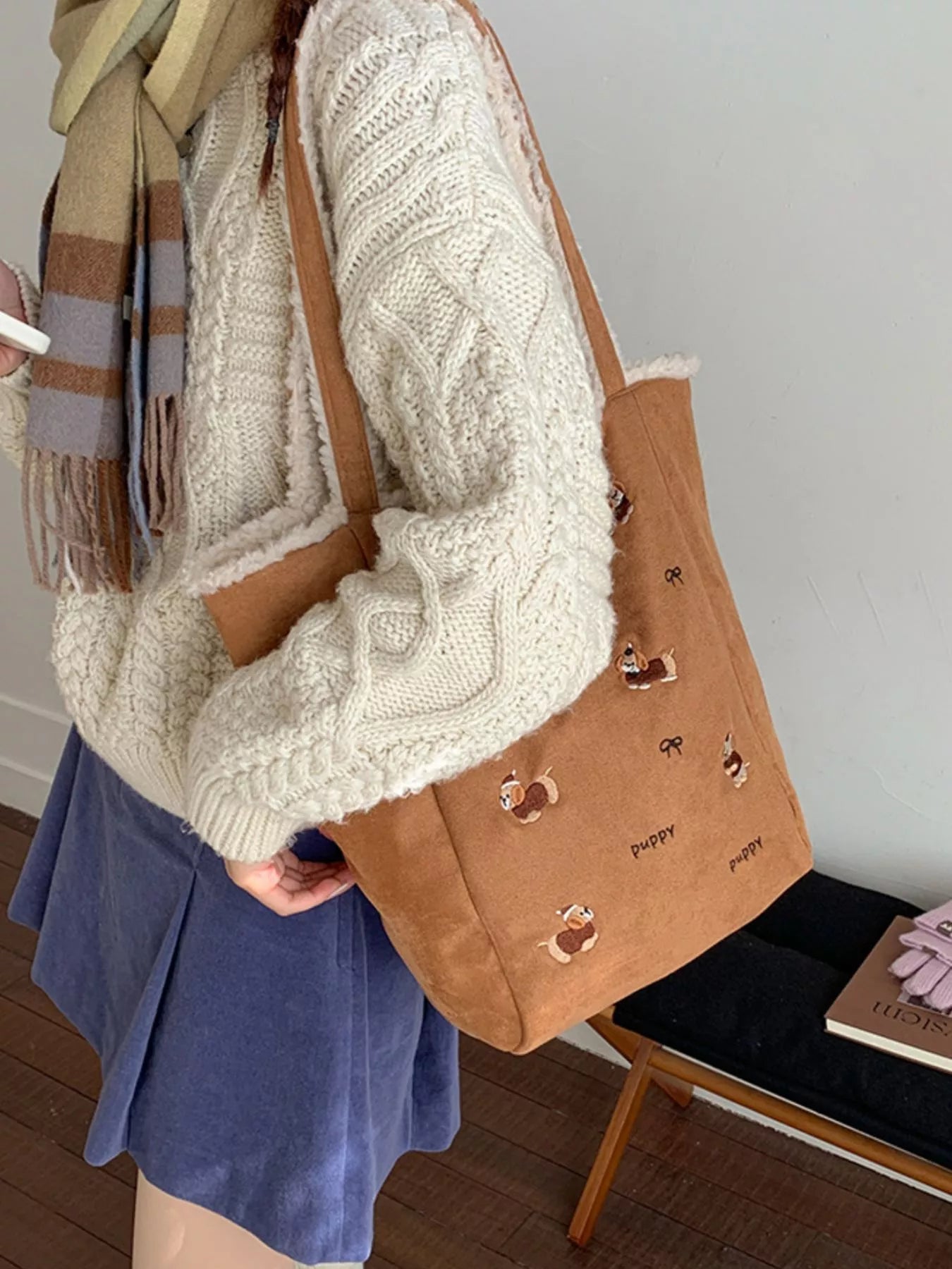 Person wearing a white knitted sweater and holding a brown tote bag with heart designs.