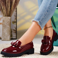 Burgundy patent leather shoes worn with light blue jeans on a blurred indoor background
