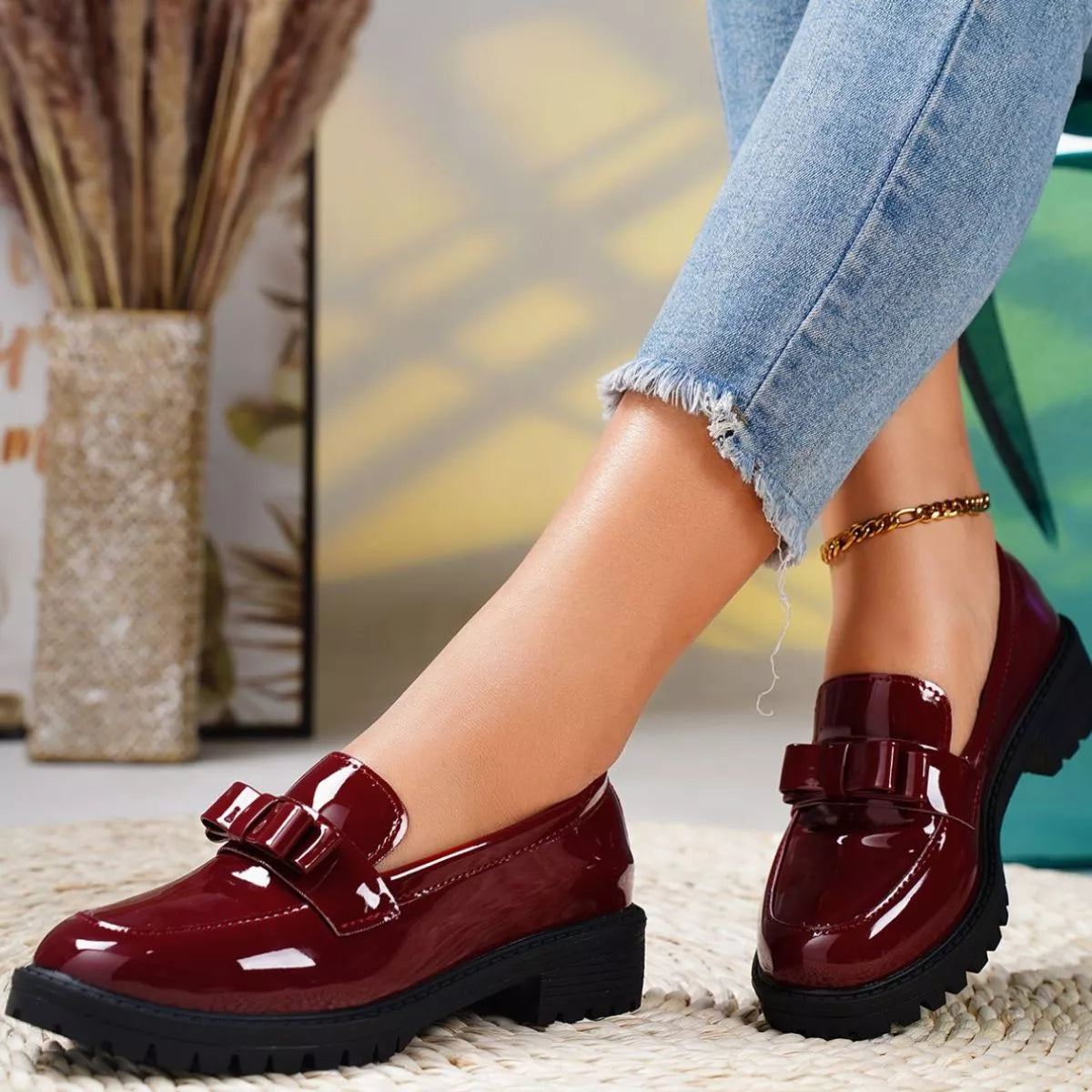 Burgundy patent leather shoes worn with light blue jeans on a blurred indoor background