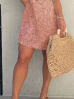 Person wearing a pink dress holding a straw bag against a plain background