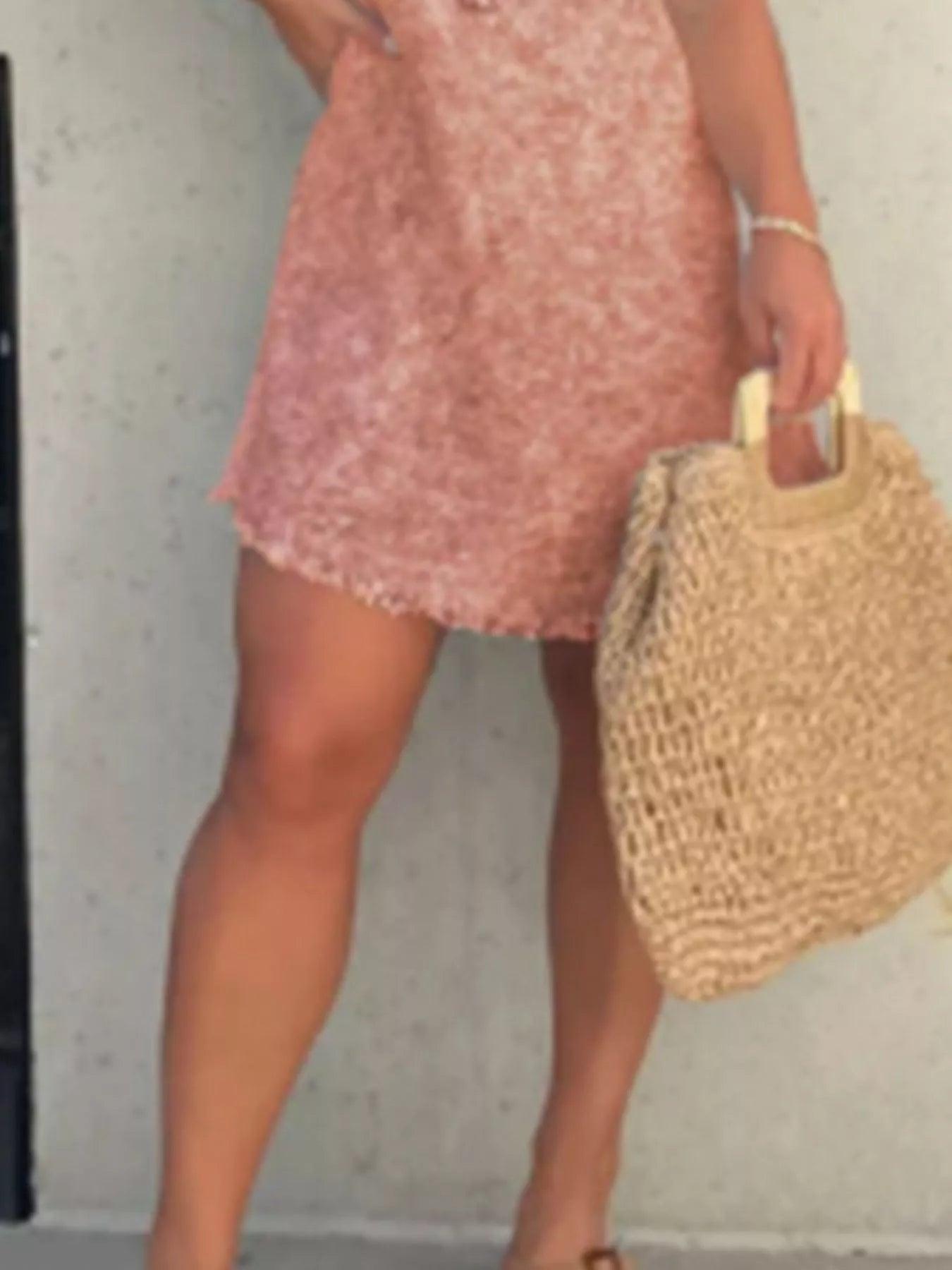Person wearing a pink dress holding a straw bag against a plain background