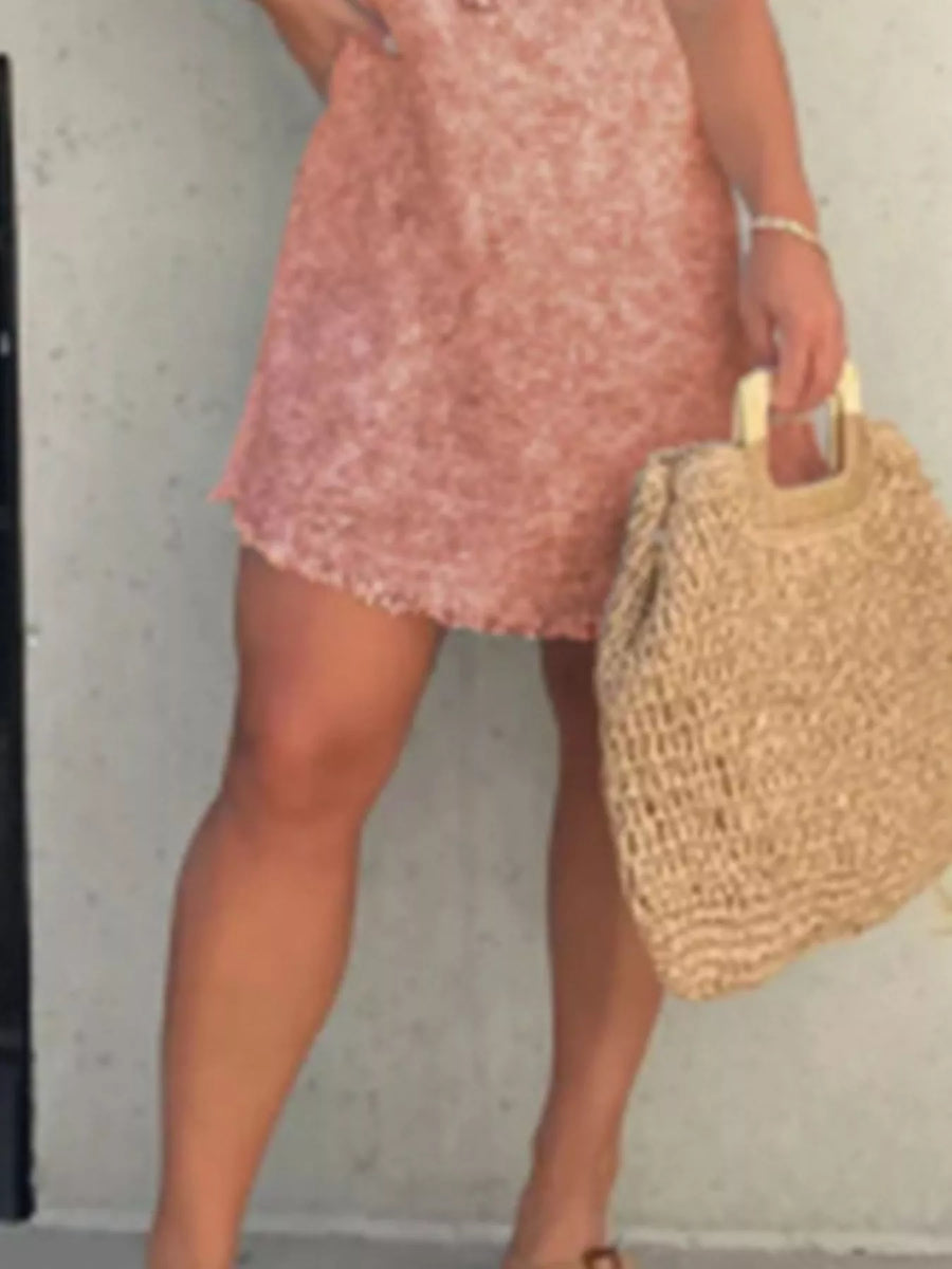 Person wearing a pink dress holding a straw bag against a plain background