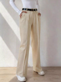 Person wearing beige wide-leg pants with a white top and black belt on a neutral background