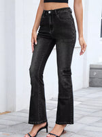 Person wearing black flared jeans standing on a stone floor with a white wall background