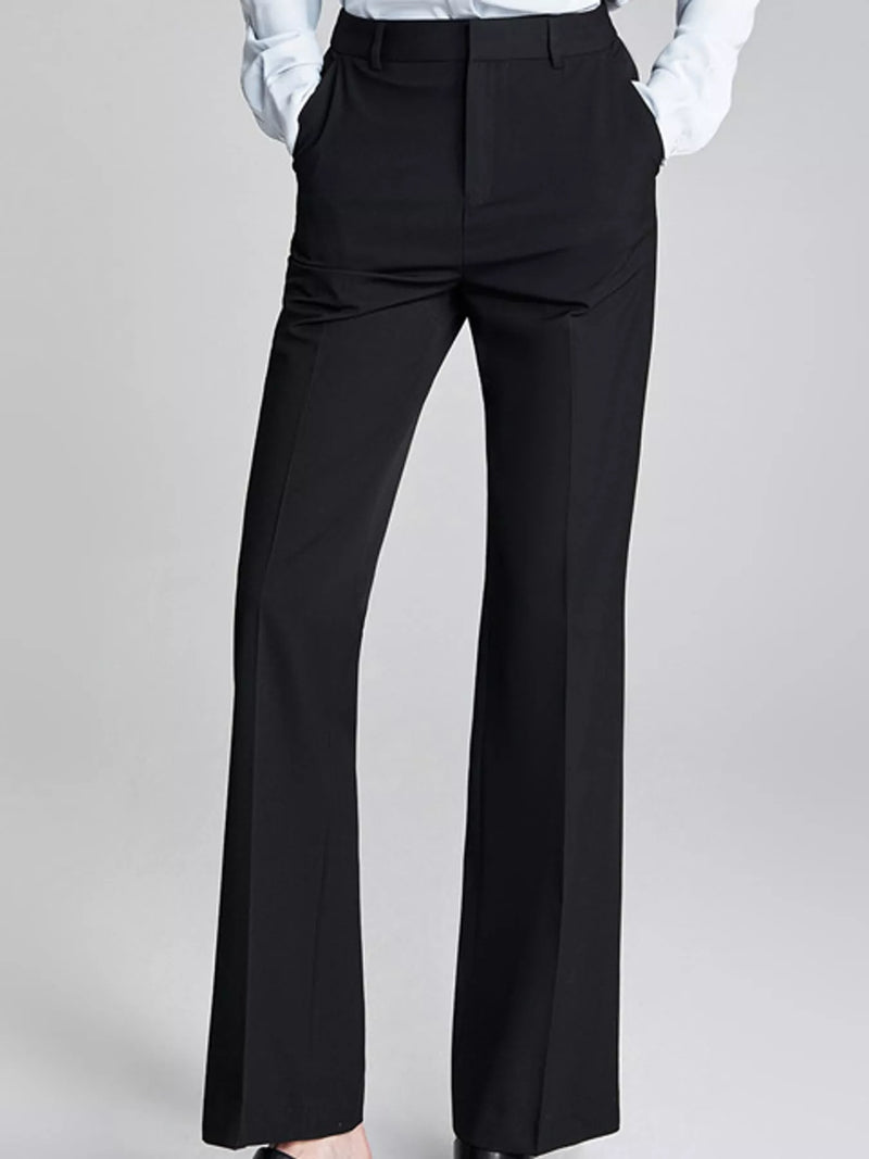 Black wide-leg trousers shown on a model from the waist down, paired with a white collared shirt, against a light gray studio background.