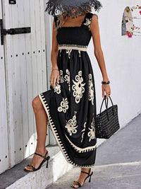Woman wearing a black dress with white patterns, standing against a white wall.