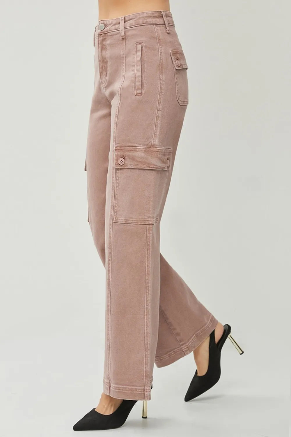 Pink cargo pants worn with black high-heeled shoes on a light gray background