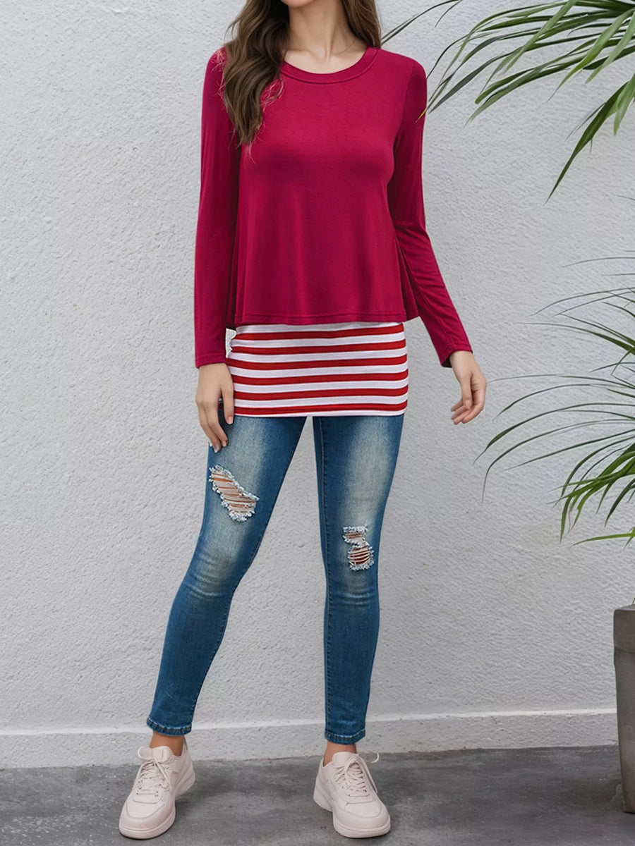 A woman modeling a two-piece outfit featuring a long-sleeve crewneck top in deep magenta and a matching mini skirt with red and white horizontal stripes, paired with distressed blue jeans and white sneakers.