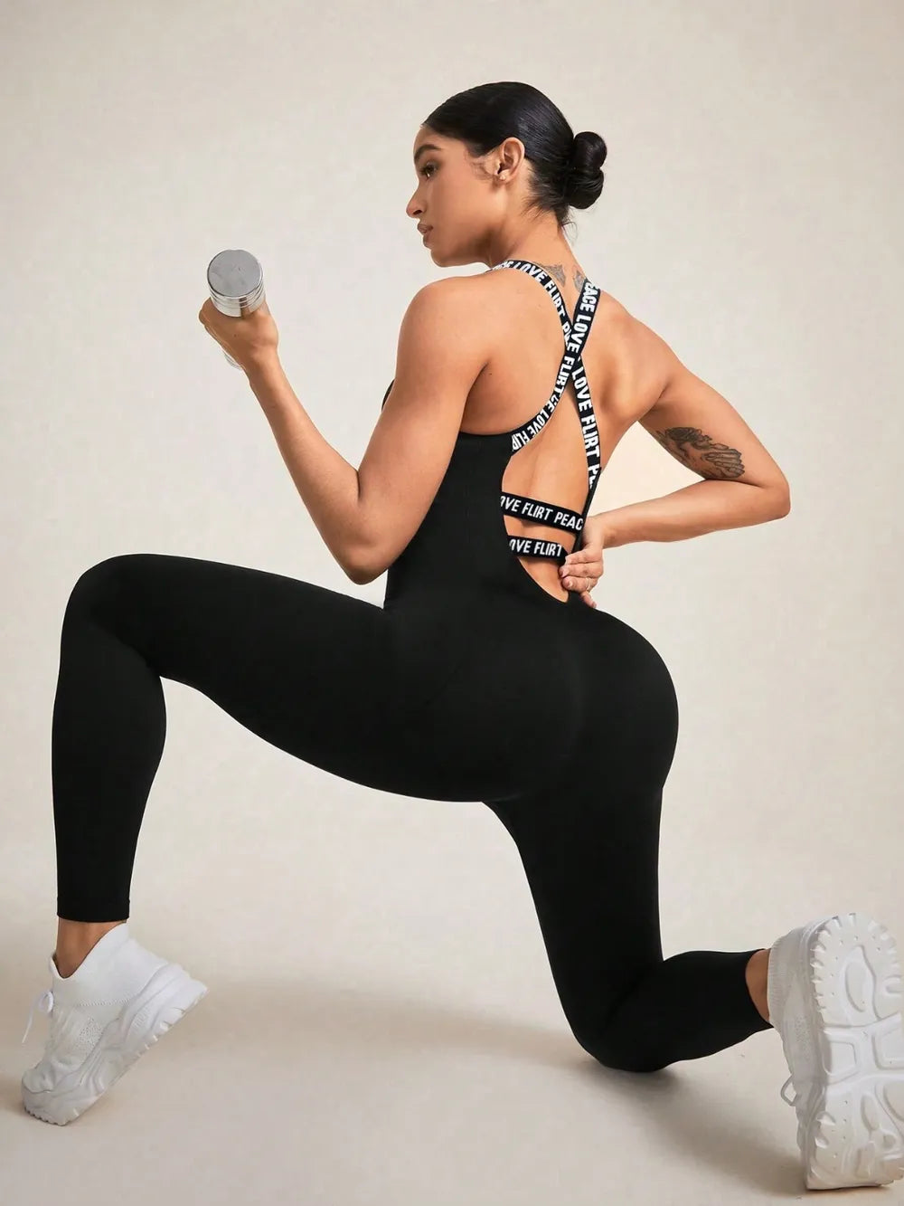 Woman in black athletic wear with visible branding, holding a dumbbell on a plain background