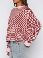 Person wearing a red and white striped shirt with pink cuffs and hem, paired with light blue jeans on a plain background.