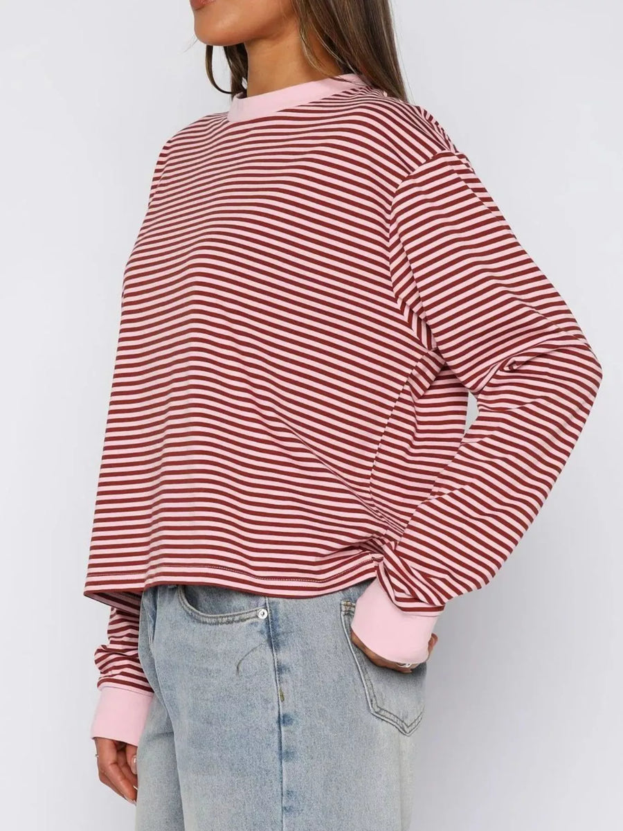 Person wearing a red and white striped shirt with pink cuffs and hem, paired with light blue jeans on a plain background.