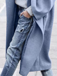 Person wearing a long blue coat over jeans with a blurred background