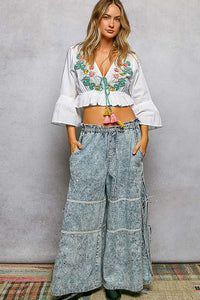 Woman wearing a white embroidered top and wide-leg jeans against a gray background