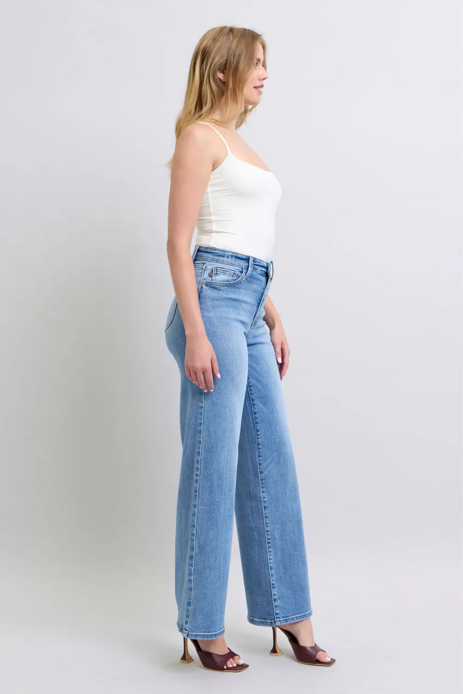 Woman wearing light blue jeans and a white top on a plain background