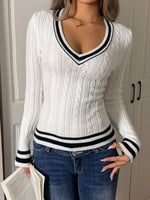 Person wearing a white sweater with black trim and blue jeans against a neutral background