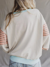 Person wearing a beige sweatshirt with striped sleeves on a neutral background