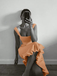 Person wearing an orange dress taking a mirror selfie against a plain wall.
