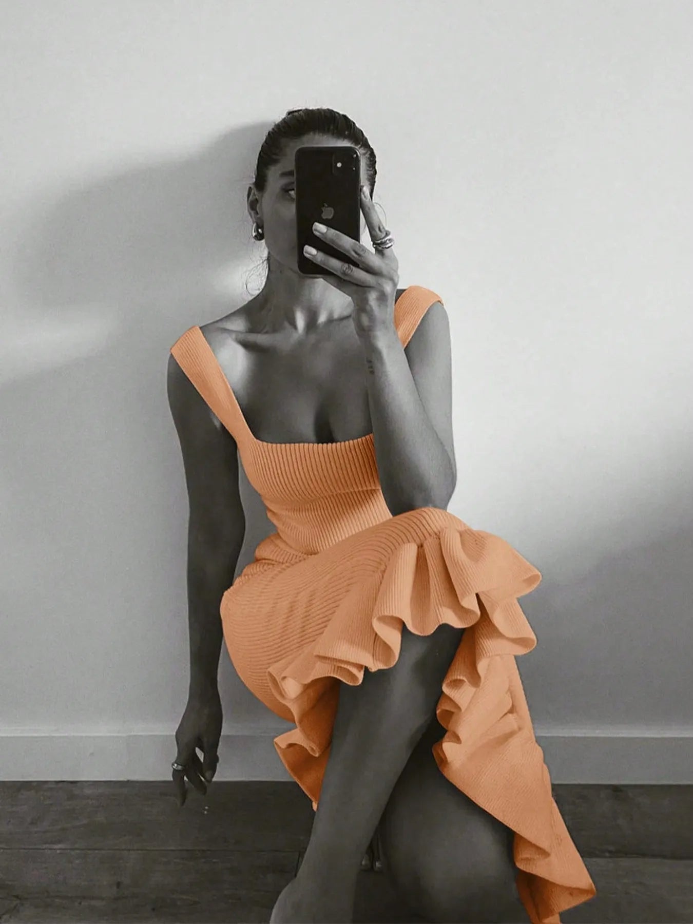 Person wearing an orange dress taking a mirror selfie against a plain wall.