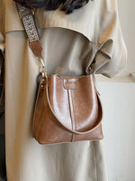 Brown leather handbag with a strap over a light-colored outfit