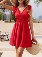 Woman in a red dress standing by a pool with palm trees and buildings in the background