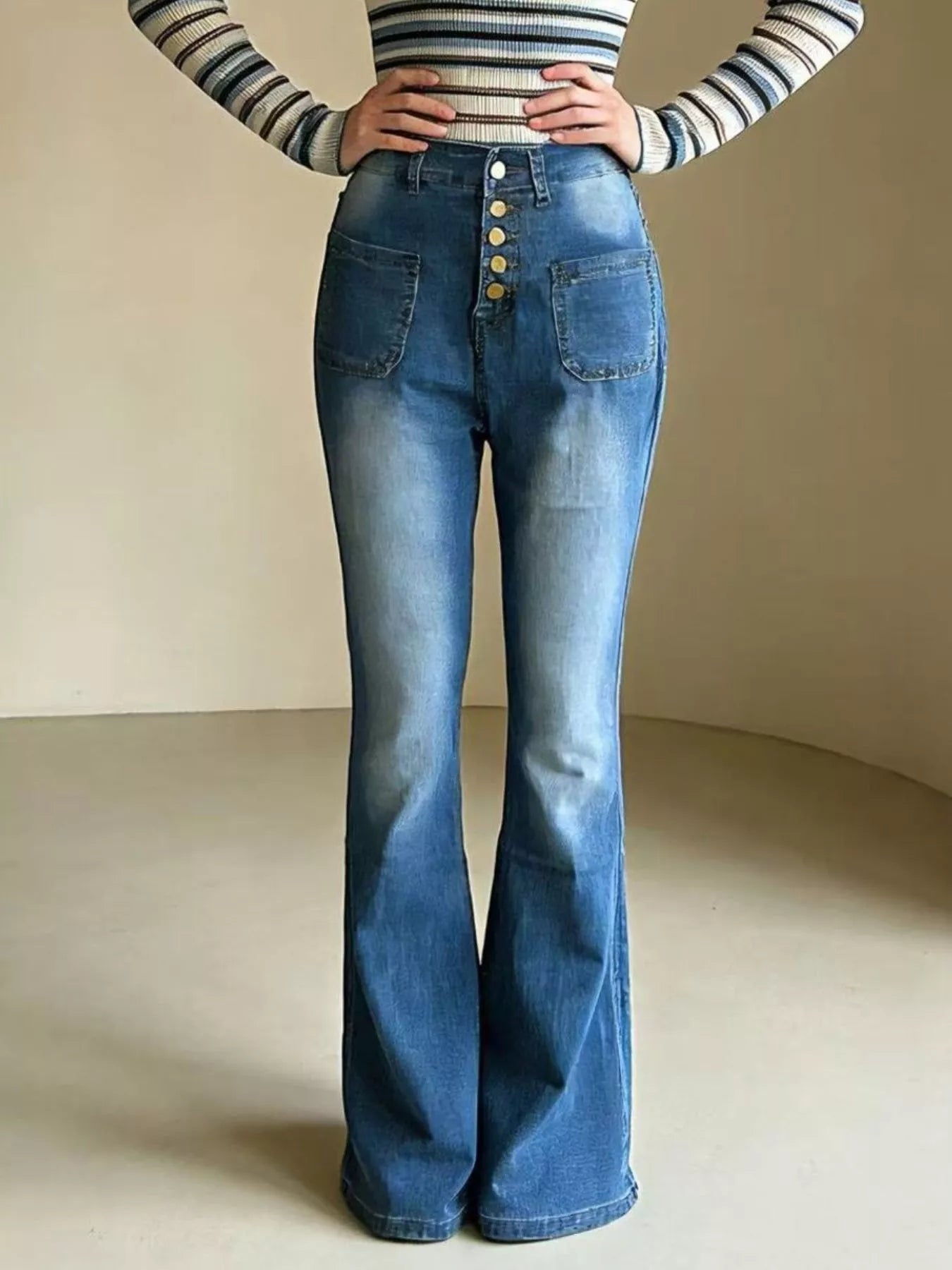 Person wearing a striped long-sleeve top and blue flared jeans on a neutral background