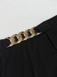 Gold chain belt on a black outfit against a white background
