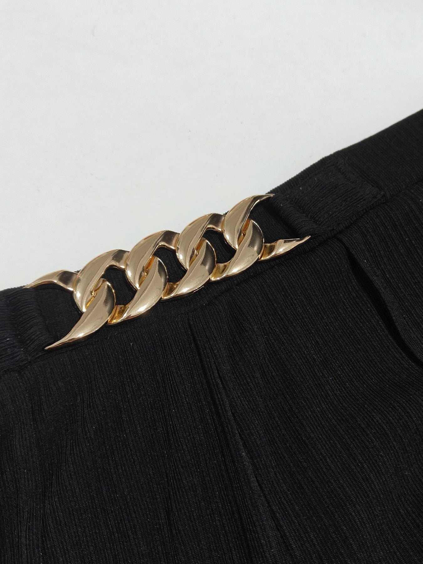 Gold chain belt on a black outfit against a white background