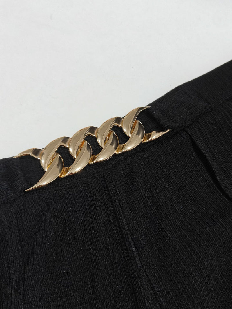 Gold chain belt on a black outfit against a white background
