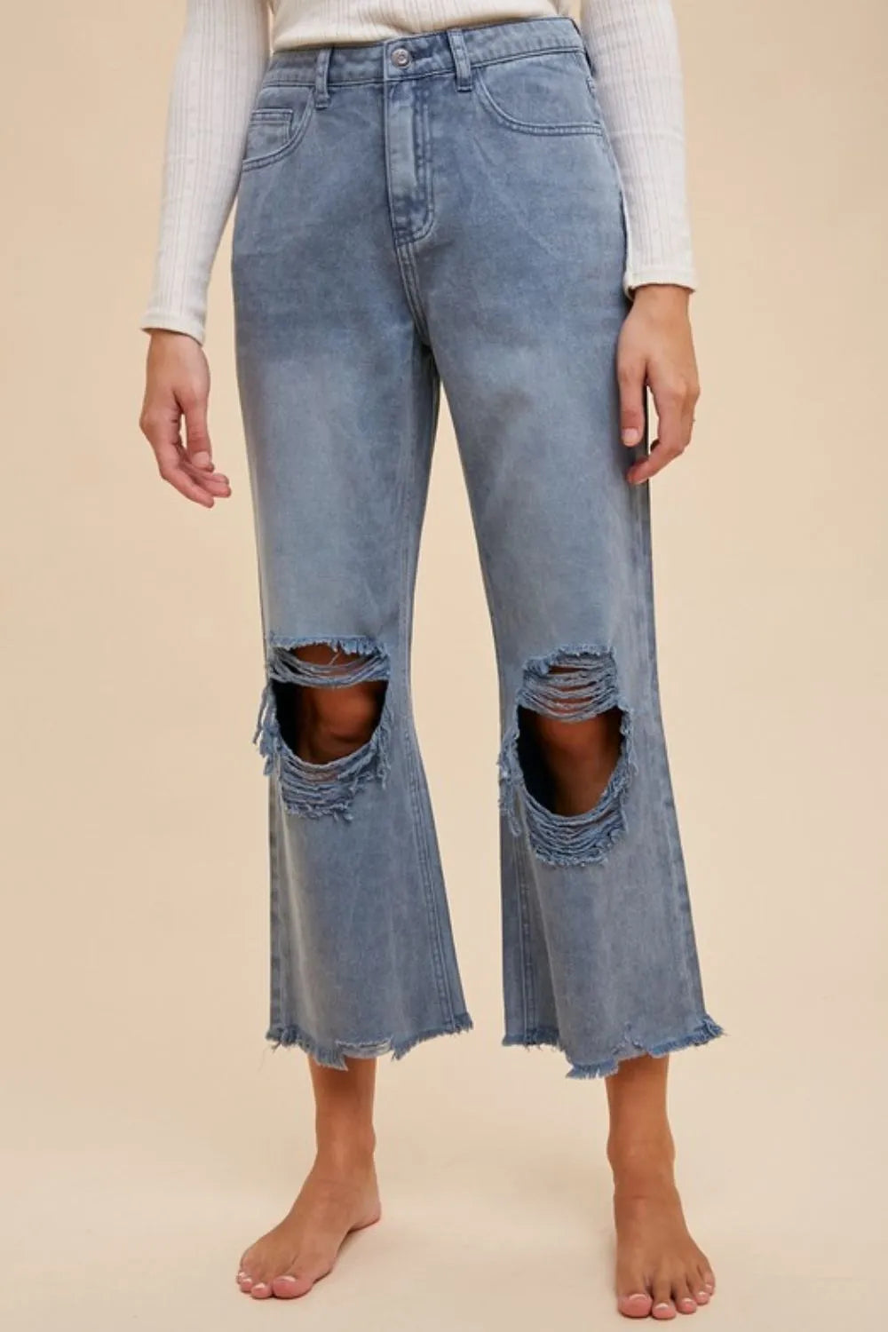 Light blue distressed jeans worn by a person on a beige background