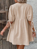 Beige dress with puff sleeves worn by a person against a wooden door and stone wall background