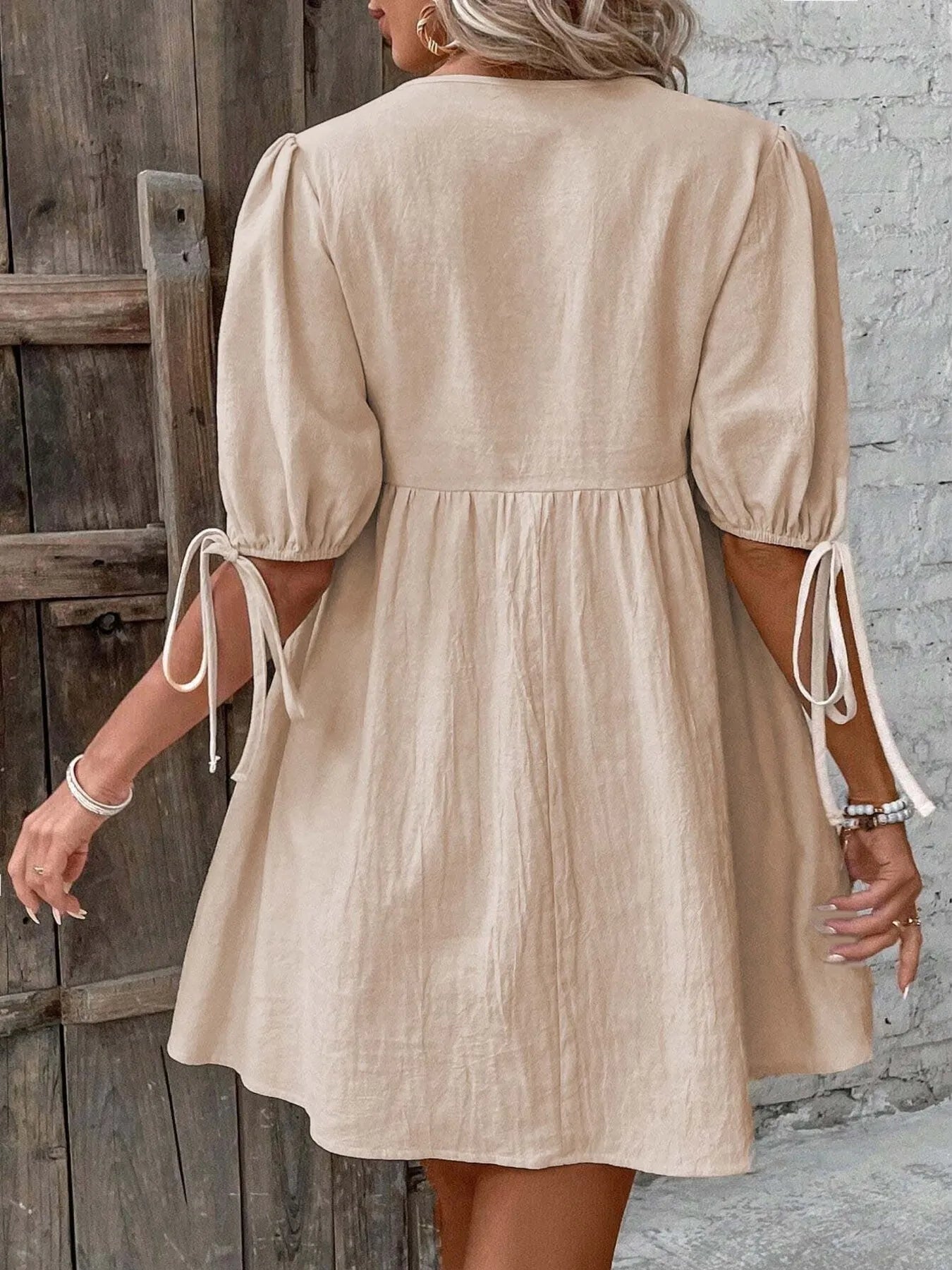 Beige dress with puff sleeves worn by a person against a wooden door and stone wall background