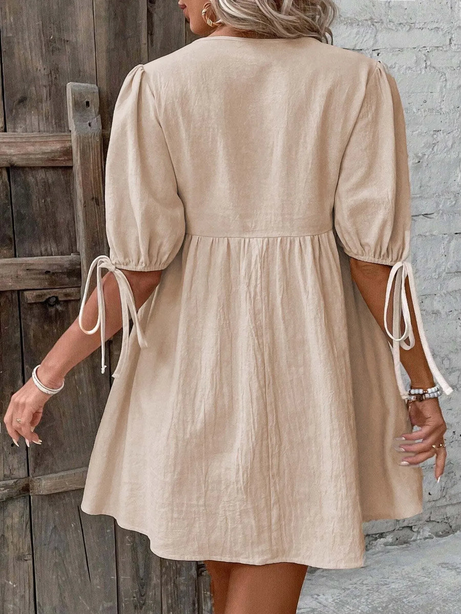 Beige dress with puff sleeves worn by a person against a wooden door and stone wall background
