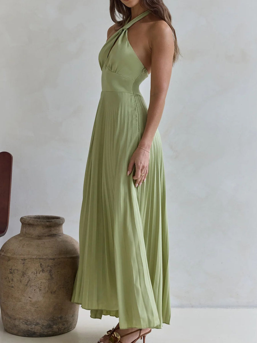 Woman wearing a green halter neck dress standing next to a large vase against a plain background
