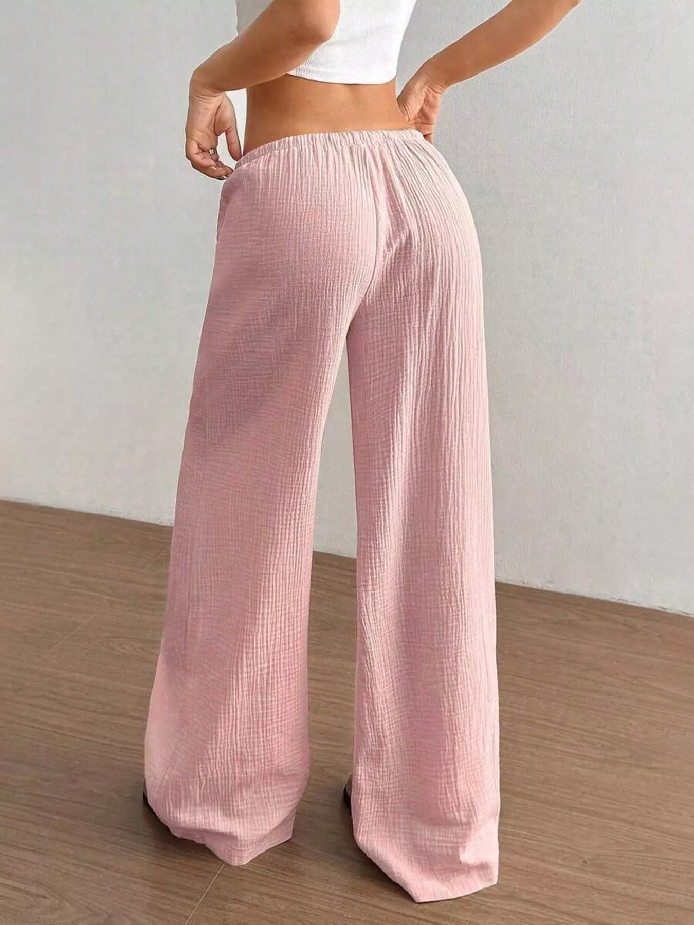 Person wearing pink corduroy pants on a wooden floor with a white wall background