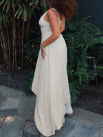 Woman in a long, light-colored dress standing outdoors with greenery in the background