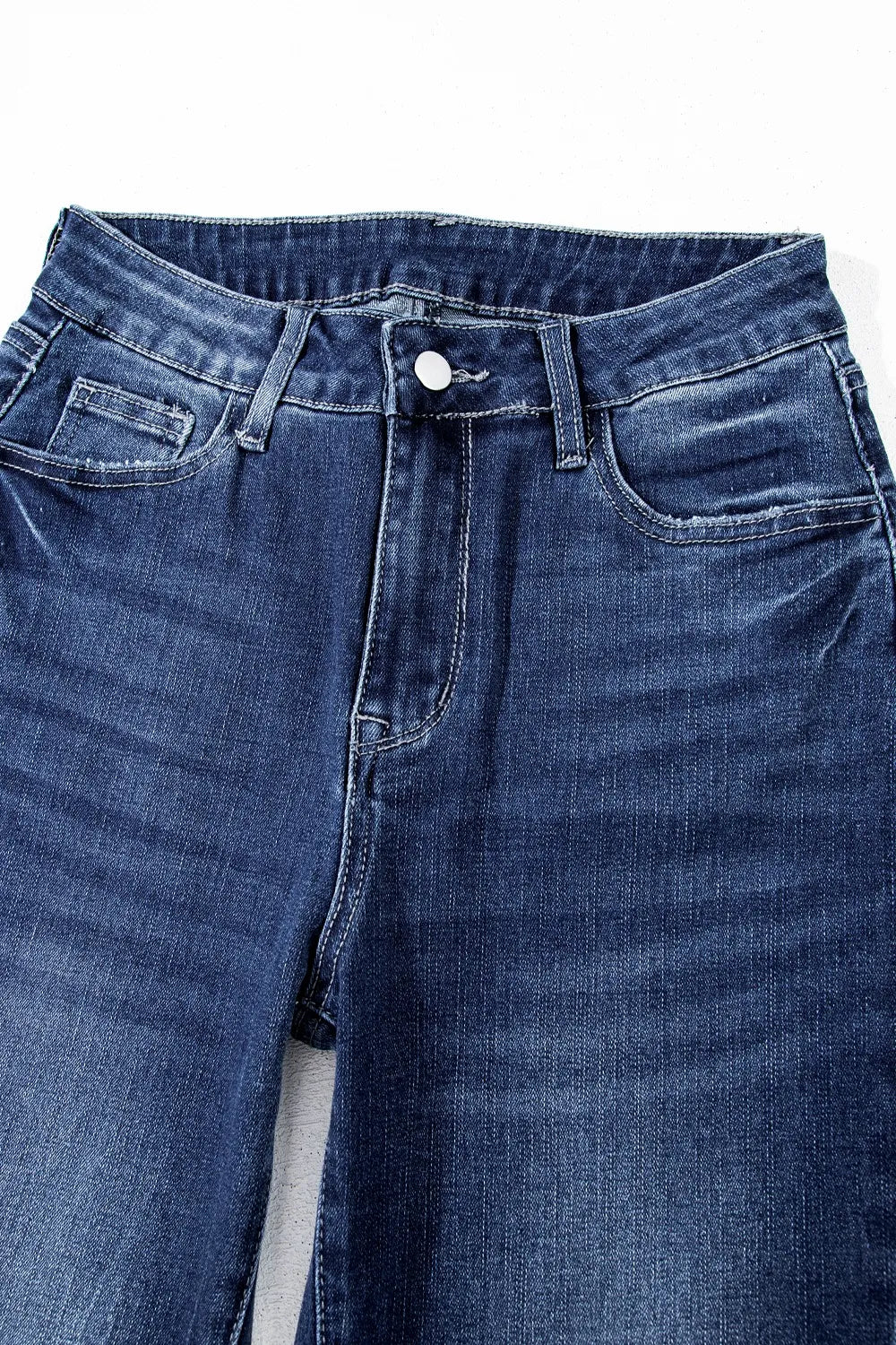 Close-up of blue jeans with a button on a white background