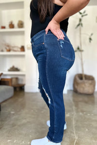 Person wearing blue jeans and a black top in a room with a white wall and a shelf.