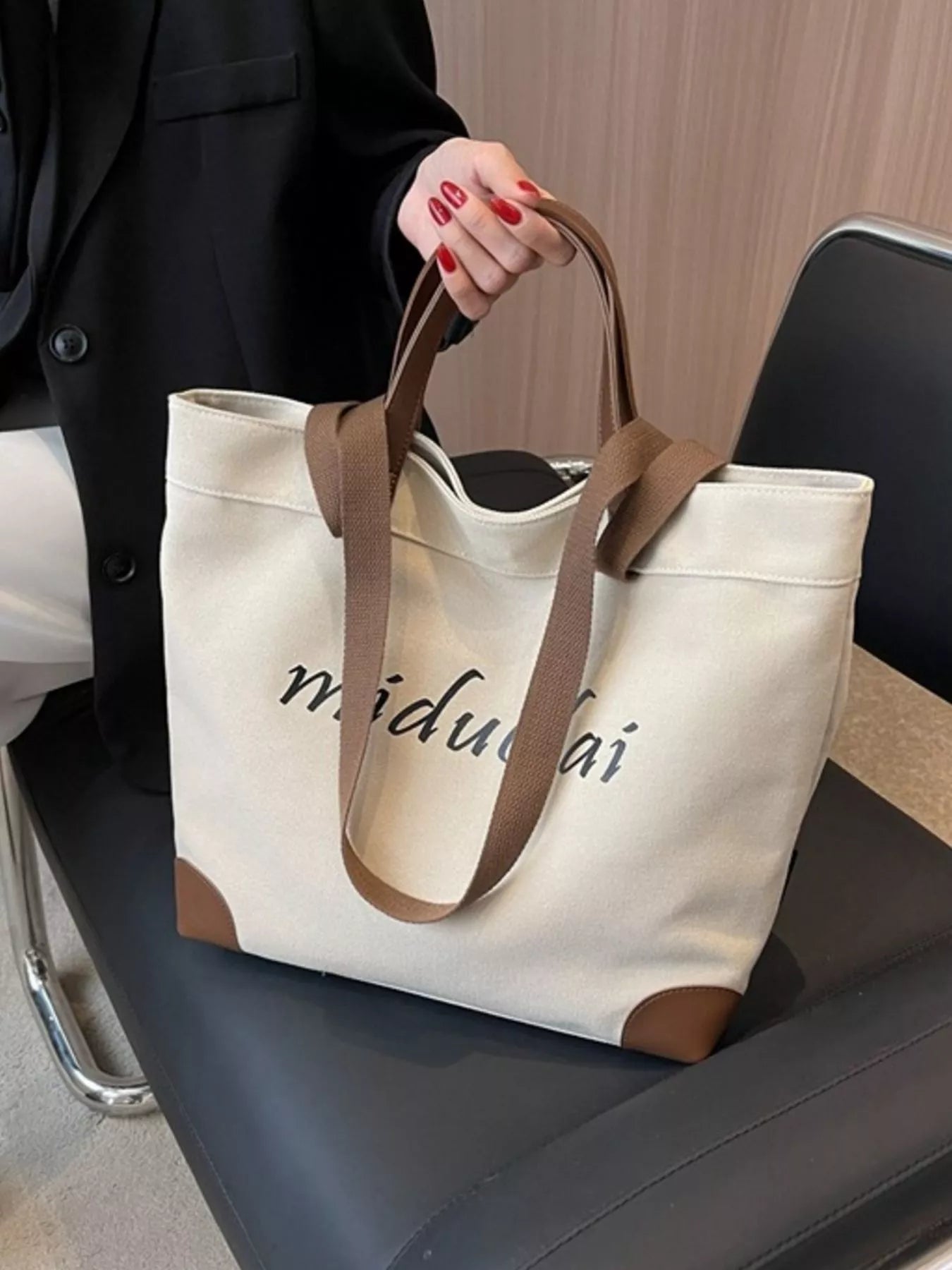 Person holding a white tote bag with brown handles on a chair.