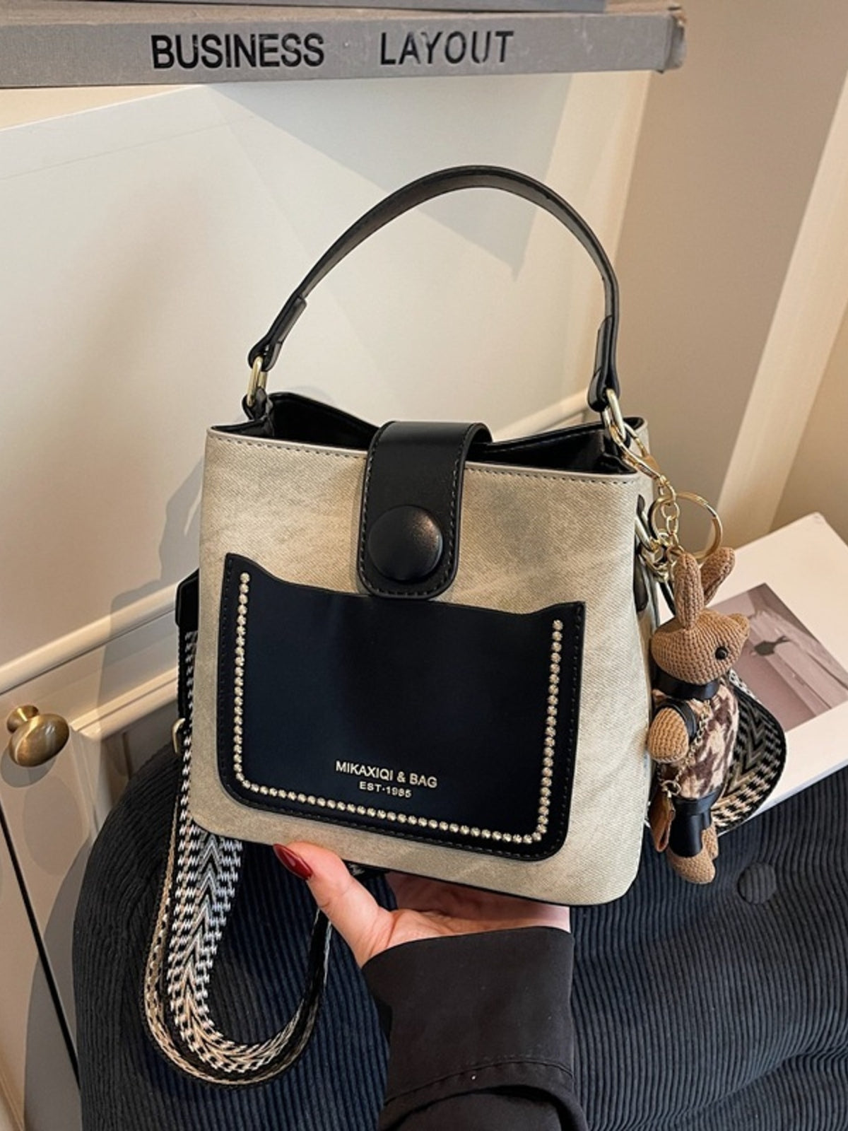Handbag with black accent and keychain held by a person, with a blurred background.