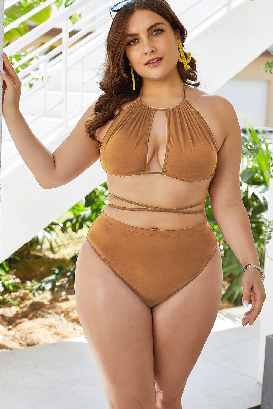 Woman wearing a brown swimsuit outdoors with greenery in the background