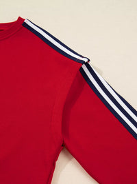Red sweatshirt with white and navy stripes on sleeves against a beige background