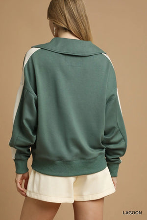 Green sweatshirt with white sleeves worn by a person on a beige background