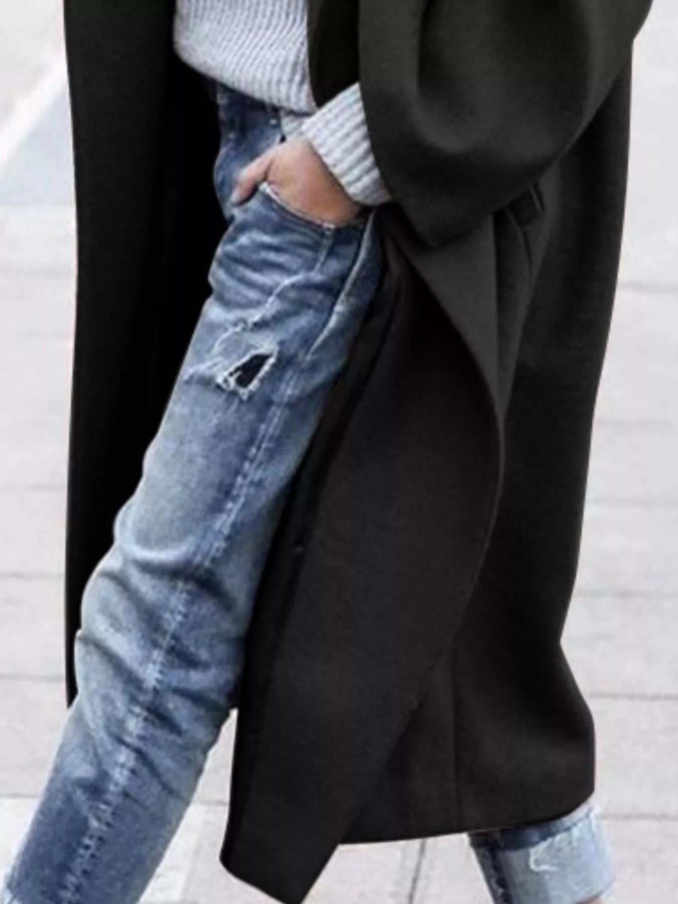 Person wearing a black coat over a light gray sweater and blue jeans on a light background