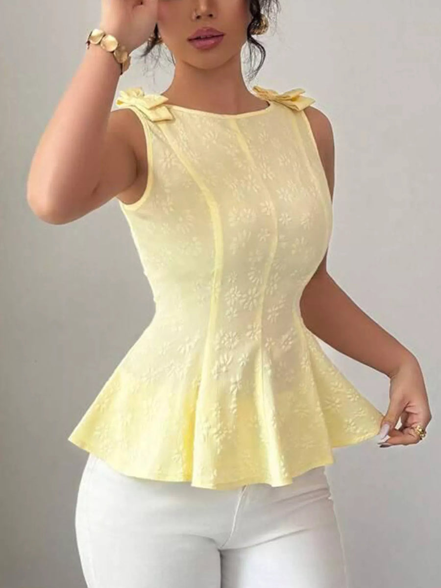 Woman wearing a yellow peplum top and white pants against a gray background